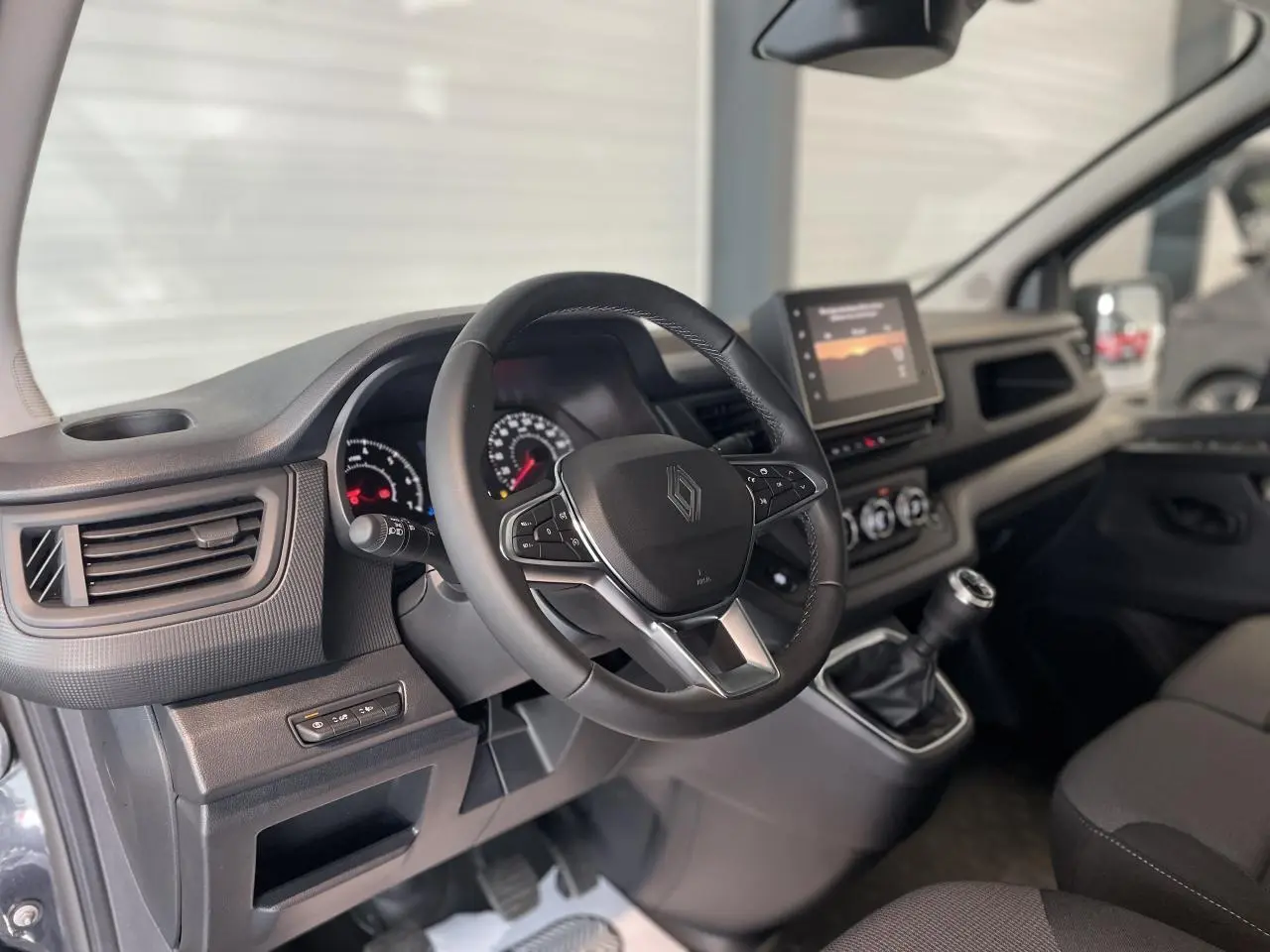 Vue intérieure côté conducteur du Renault Trafic Fourgon gris Comète, montrant le volant, tableau de bord et écran tactile central.