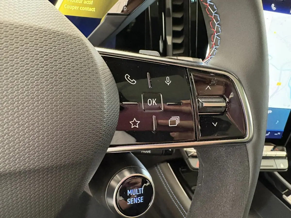 Gros plan sur le volant en suède et cuir avec commandes multifonctions et surpiqûres tricolores du Renault Espace blanc 2025.