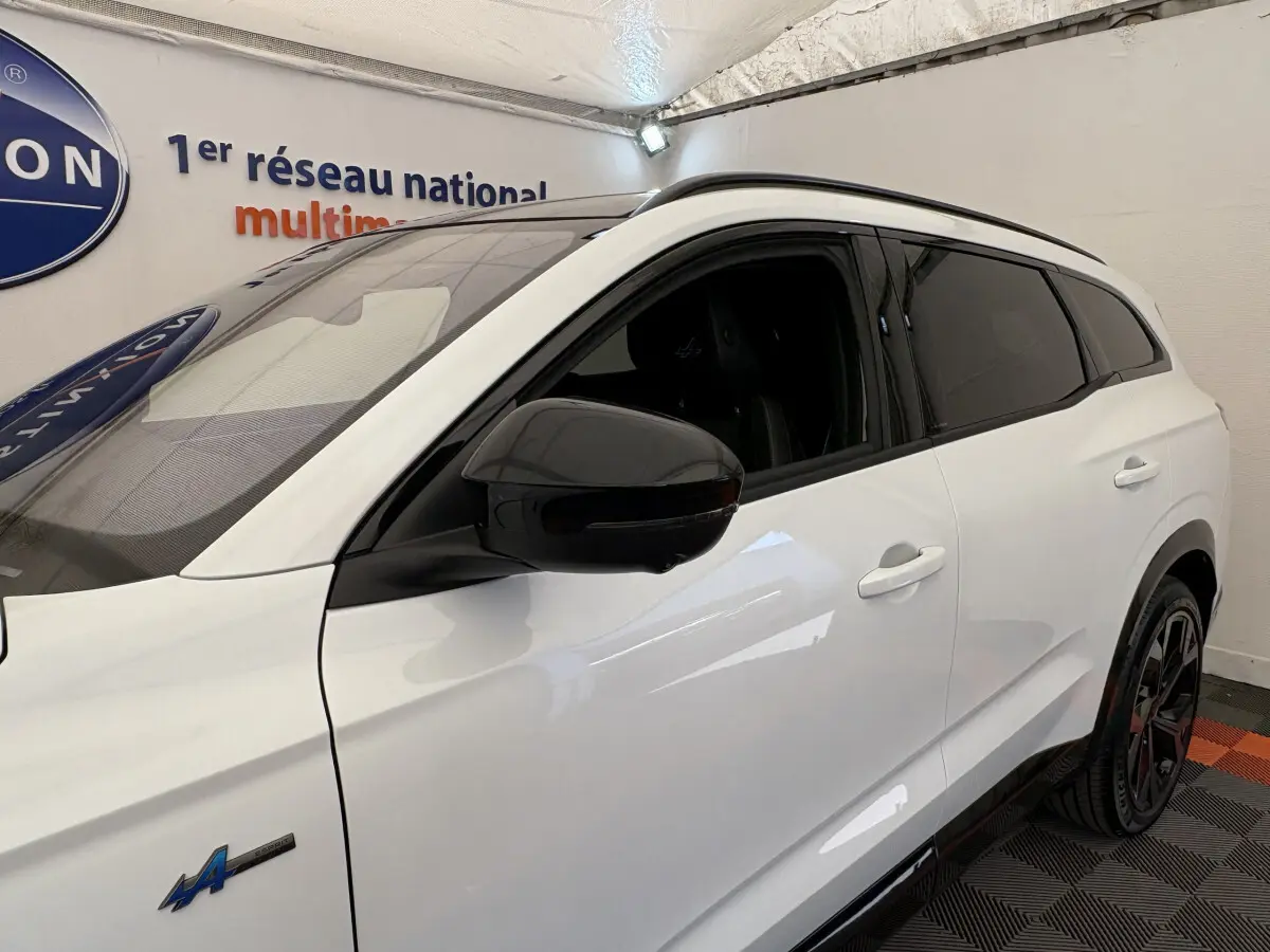 Vue de côté droit avant d’un Renault Espace blanc esprit Alpine avec rétroviseur noir et vitres teintées en intérieur showroom.