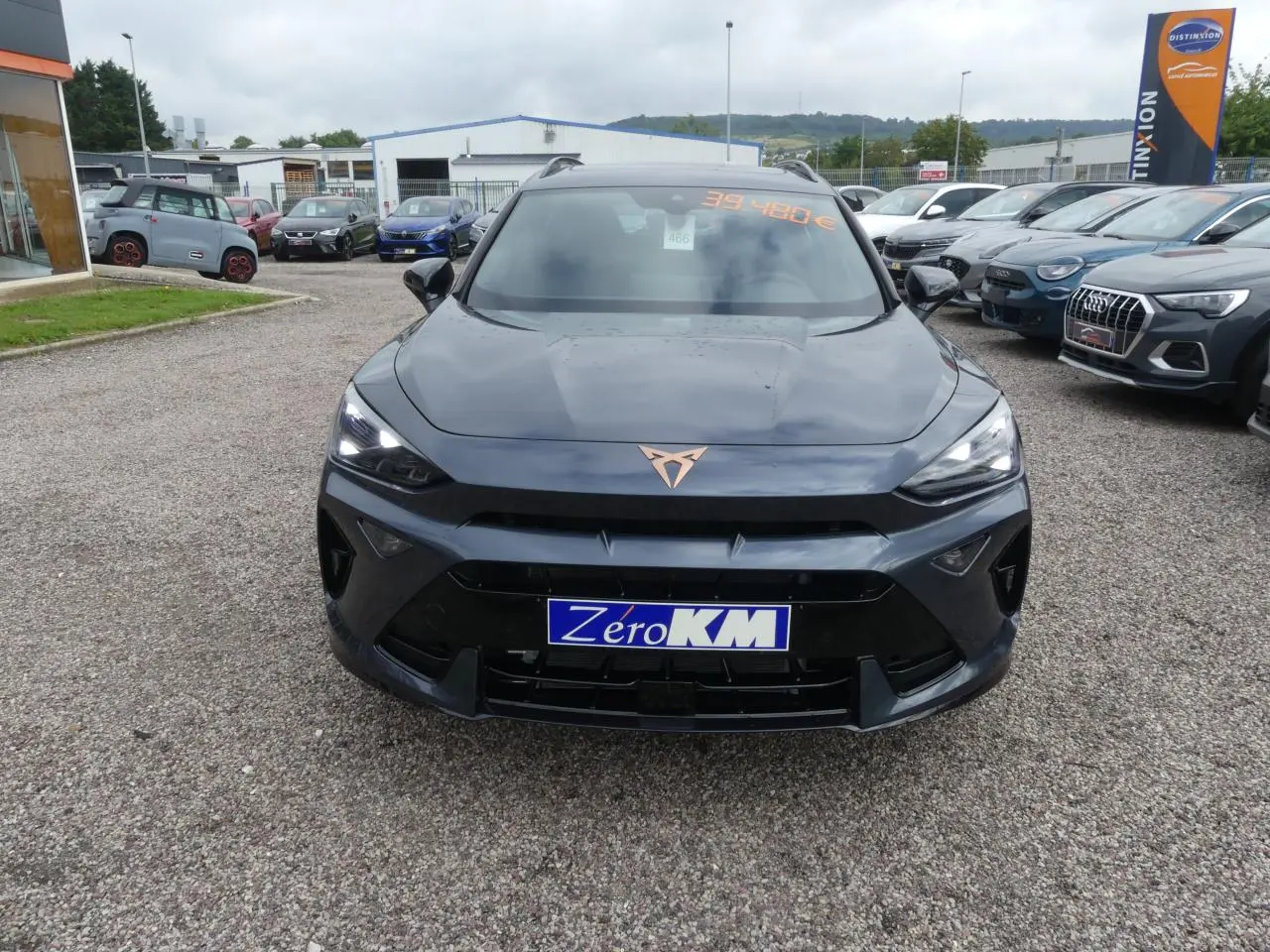Vue avant d'un CUPRA Formentor gris magnétique avec logo cuivré et calandre noire sur un parking extérieur.