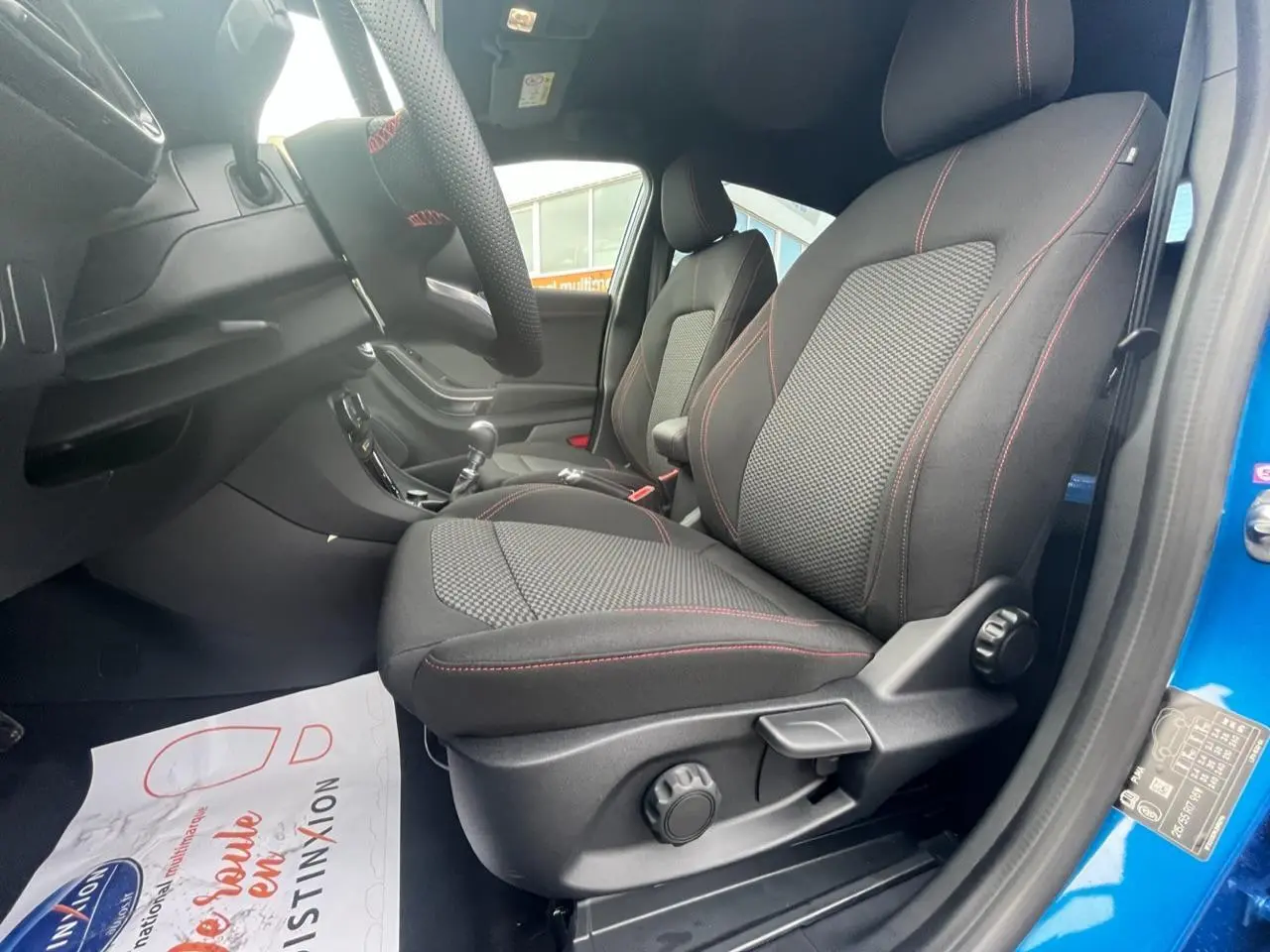 Intérieur du Ford Puma 2022 bleu, vue côté droit sur sièges avant noirs avec surpiqûres rouges et volant.