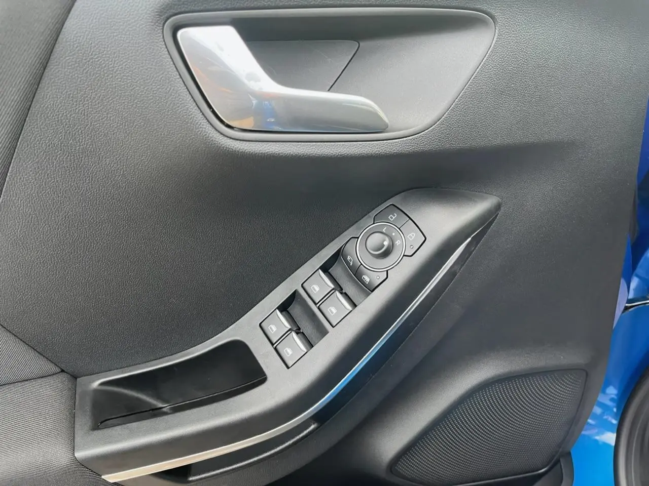 Gros plan sur la porte côté conducteur du Ford Puma bleu, montrant les commandes électriques des vitres et le bouton de réglage des rétroviseurs.
