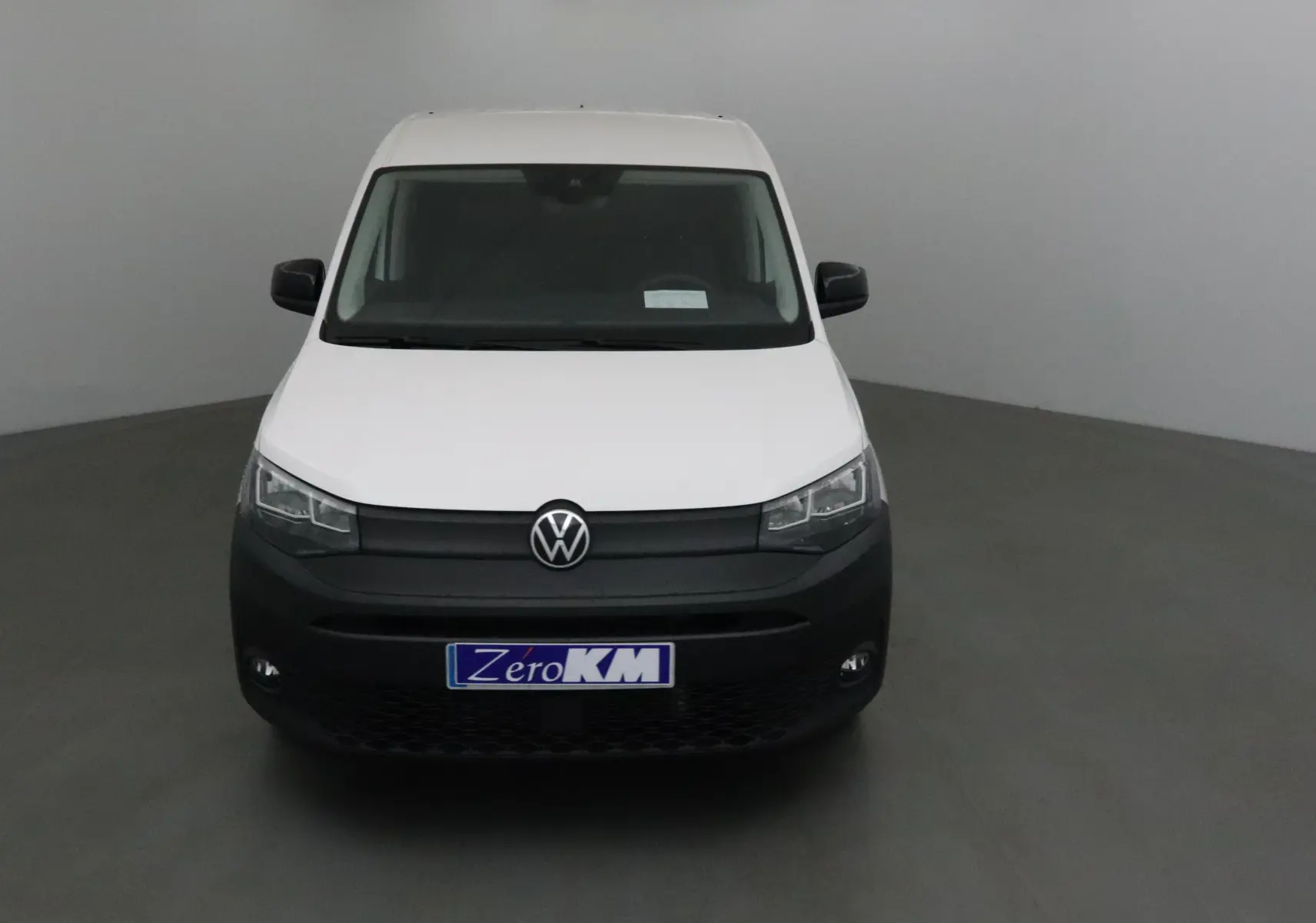 Vue frontale d'un Volkswagen Caddy Maxi blanc avec pare-chocs noir mat et plaque "Zero KM" visible.