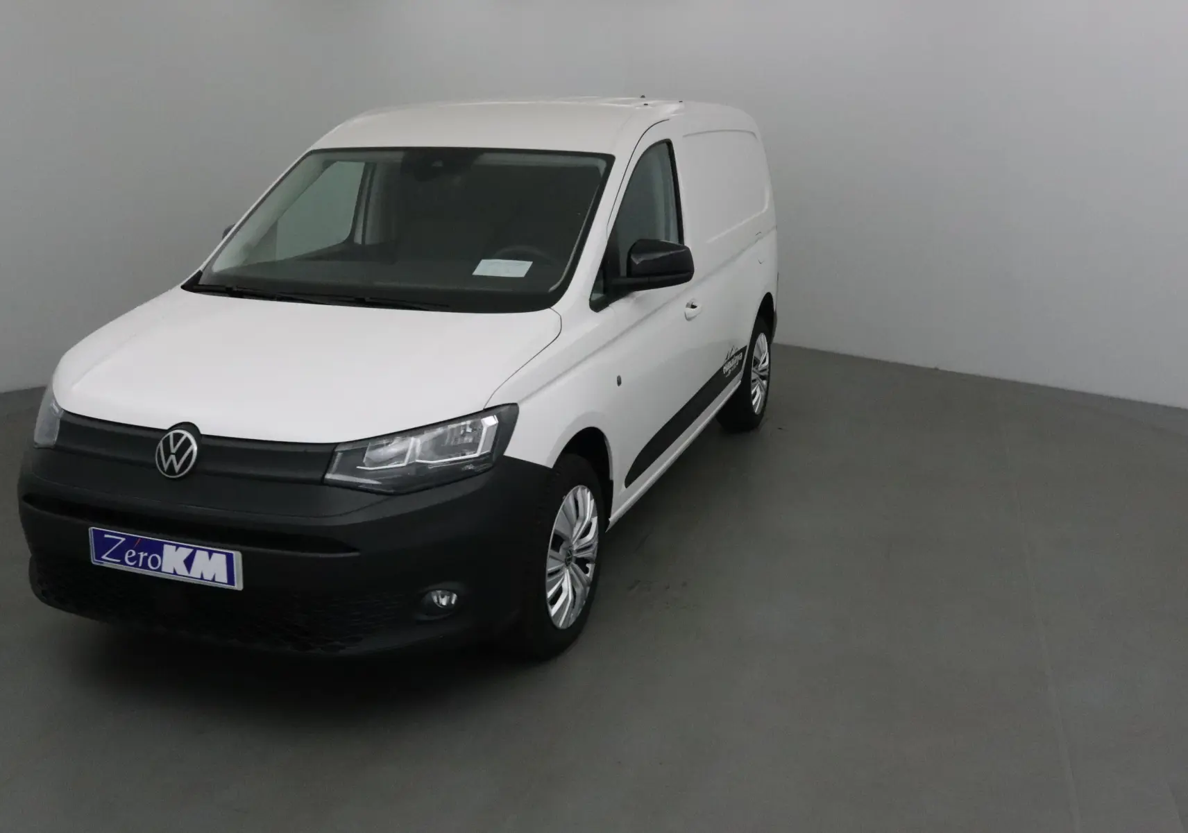 Volkswagen Caddy Maxi blanc en 3/4 avant droit avec pare-chocs noir et logo VW bien visible.
