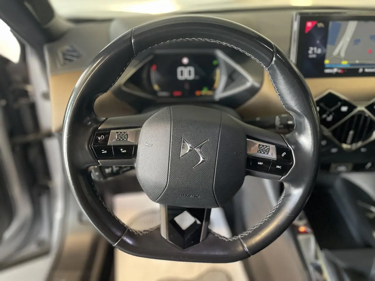 Vue rapprochée du volant en cuir noir du DS3 Crossback avec commandes intégrées et tableau de bord numérique en arrière-plan.