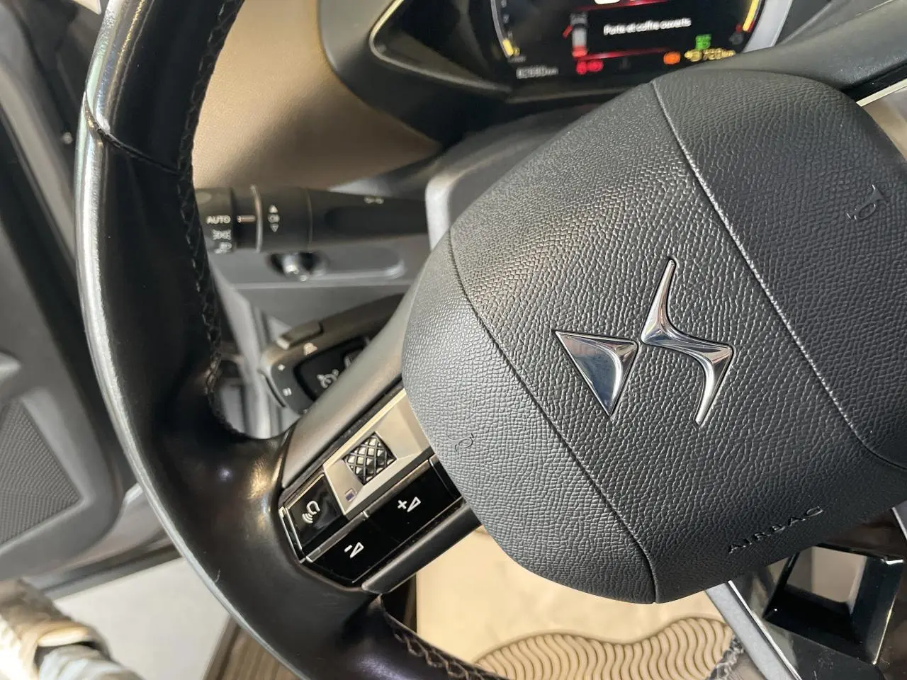 Gros plan sur le volant noir en cuir avec logo DS du DS3 Crossback 1.5 BlueHDi, intérieur beige visible en arrière-plan.