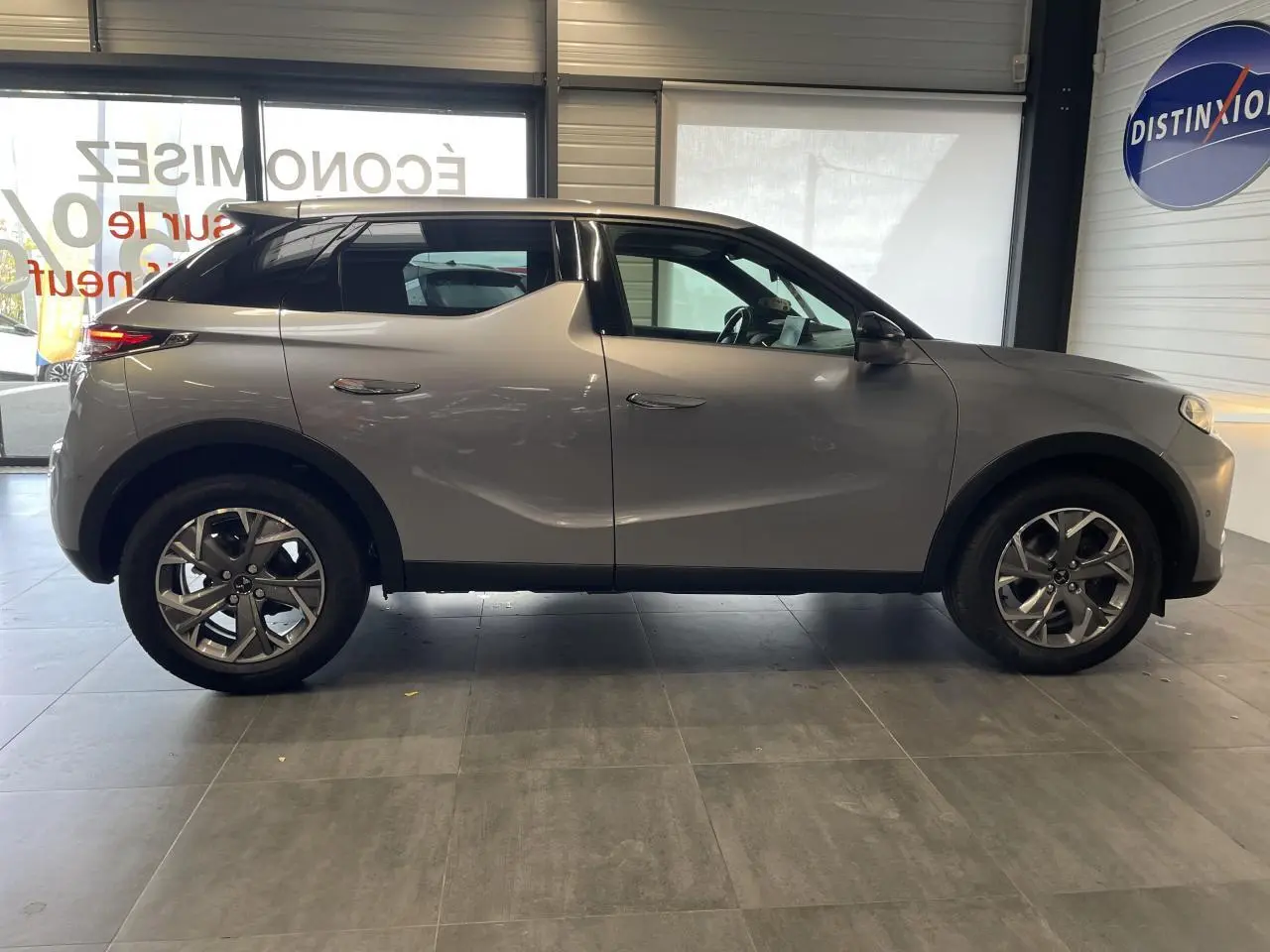 Profil côté gauche du DS3 Crossback gris Artense avec jantes alliage et toit noir en intérieur showroom.