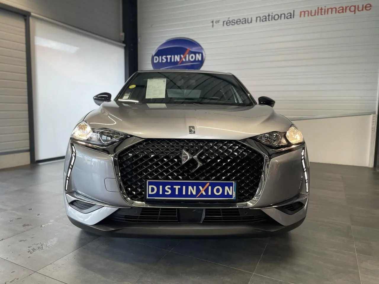 Vue de face du DS3 Crossback gris Artense, mettant en valeur sa calandre noire distinctive et ses phares allumés.