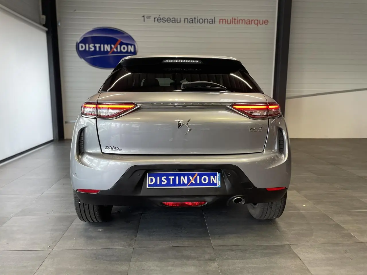 Vue arrière d'une DS3 Crossback gris Artense avec feux LED allumés et toit noir en showroom.