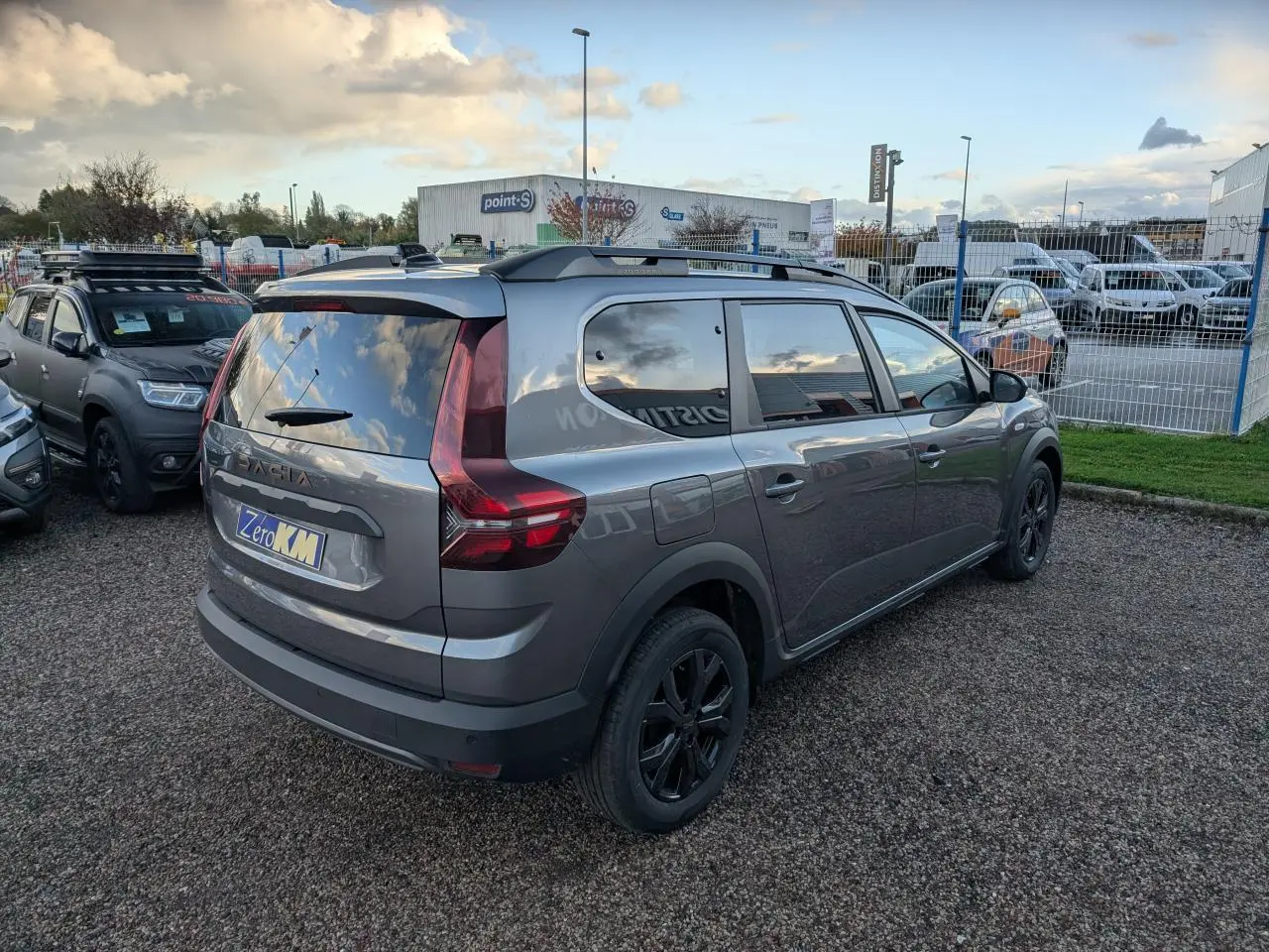 Vue 3/4 arrière droite d'un Dacia Jogger gris métallisé avec jantes noires et barres de toit.
