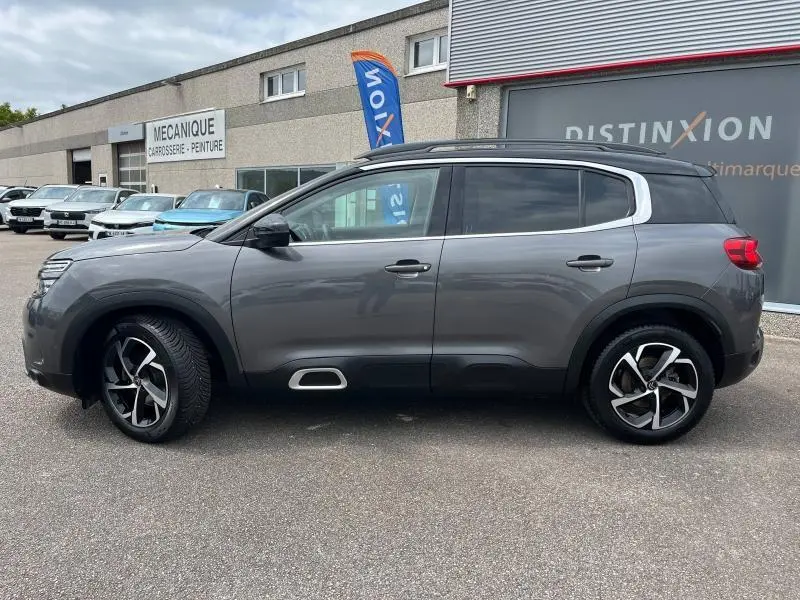 Profil droit d'un Citroën C5 Aircross gris acier 2021 avec jantes alliage et barres de toit noires visibles.