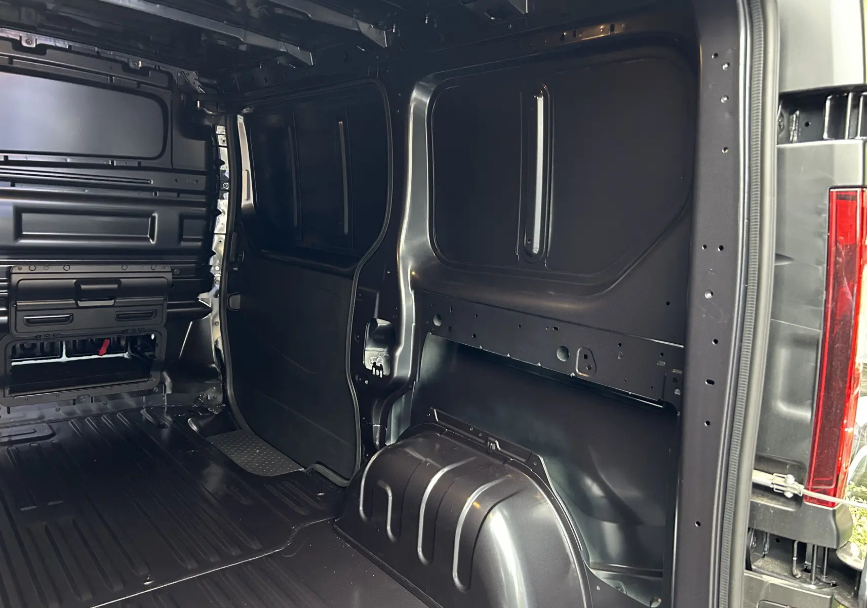 Vue intérieure arrière du Renault Trafic Fourgon gris Comète montrant l'espace de chargement vide et les parois métalliques.