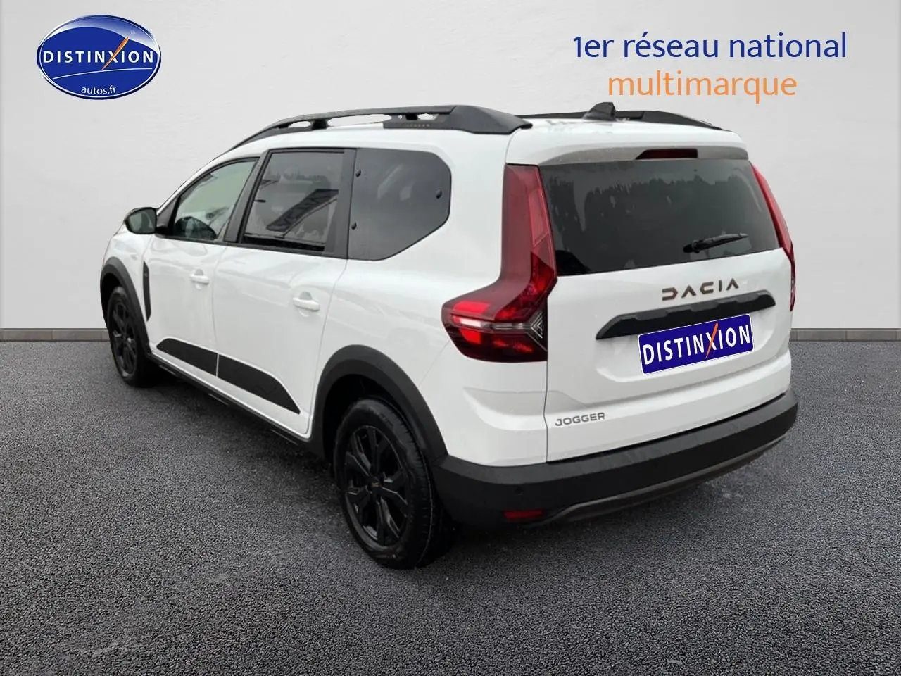 Vue 3/4 arrière droite d'un Dacia Jogger blanc 7 places avec barres de toit et jantes noires.