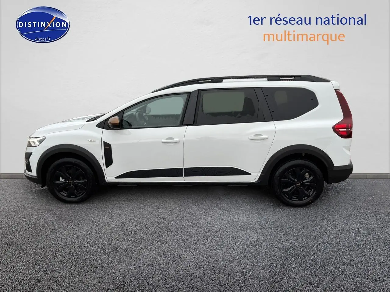 Vue de profil côté gauche d'un Dacia Jogger blanc 2025 avec jantes noires et barres de toit noires.