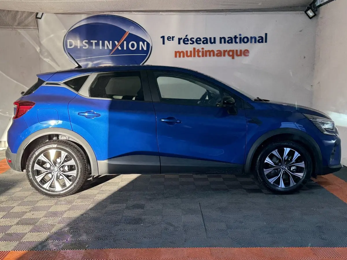 Profil droit d'un Renault Captur bleu 2024 avec jantes alliage et toit noir dans un showroom intérieur.