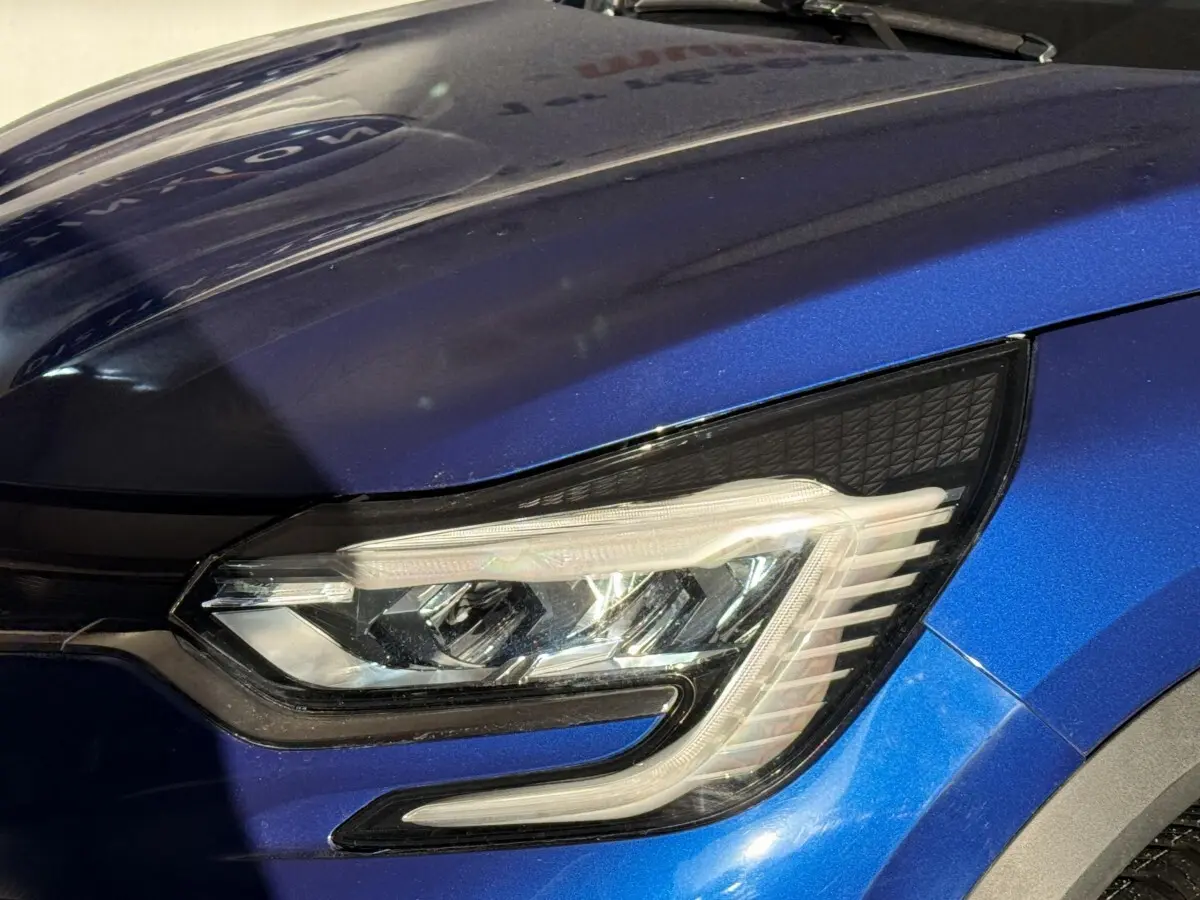 Gros plan sur le phare avant droit du Renault Captur bleu 2024 avec détails LED et carrosserie métallisée.