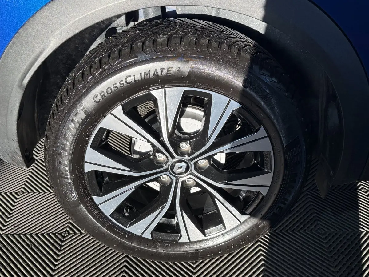 Gros plan sur la roue avant droite du Renault Captur bleu 2024 avec jante alliage bicolore et pneu Michelin CrossClimate.