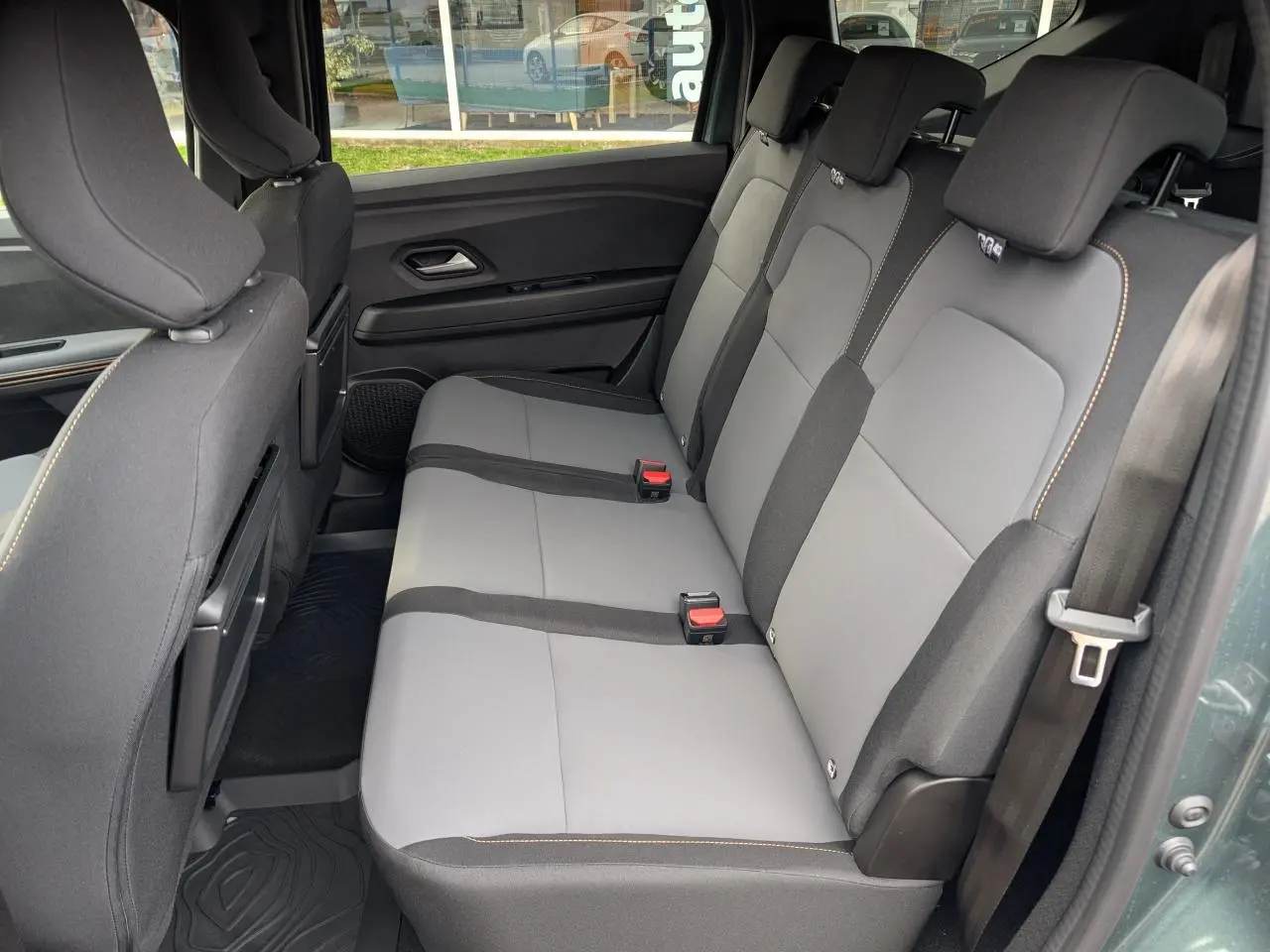 Vue latérale droite de la banquette arrière grise et noire du Dacia Jogger 2025 avec surpiqûres brun cuivré et ceintures de sécurité.