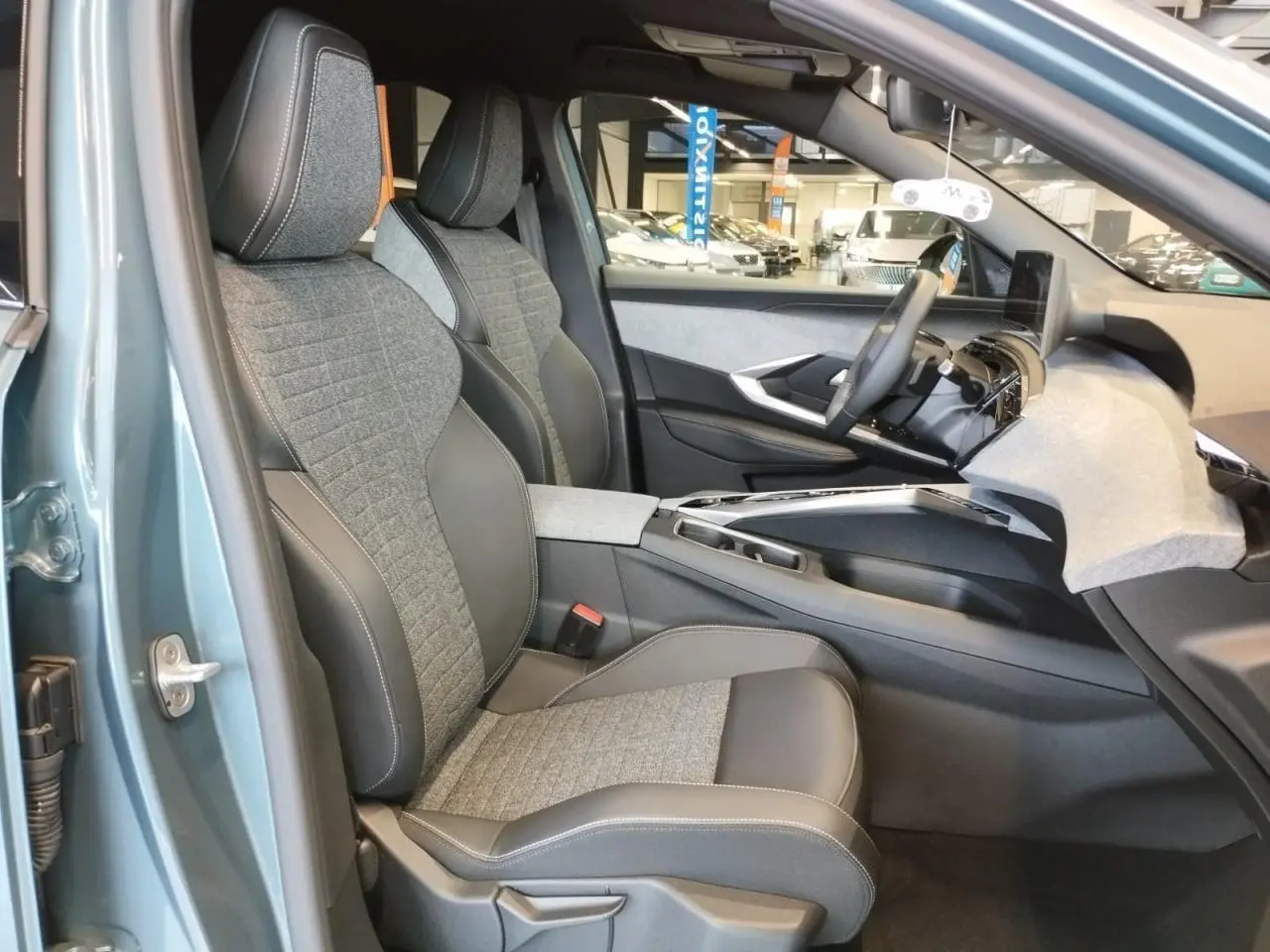 Vue intérieure côté gauche du Peugeot 3008 Bleu Azur 2025, sièges tissu gris et cuir noir avec tableau de bord moderne.
