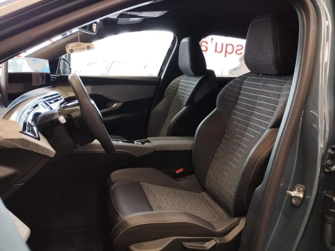 Vue intérieure côté conducteur du Peugeot 3008 2025 avec sièges tissu gris et cuir noir, planche de bord moderne et écran flottant.