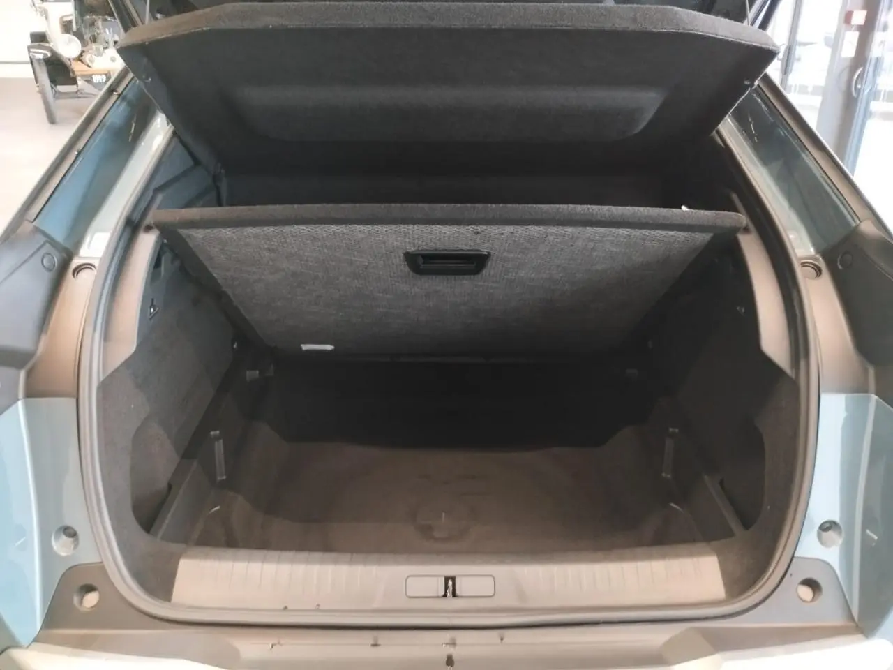 Coffre ouvert vu de l'arrière d'un Peugeot 3008 bleu Azul avec cache-bagages relevé et intérieur noir.