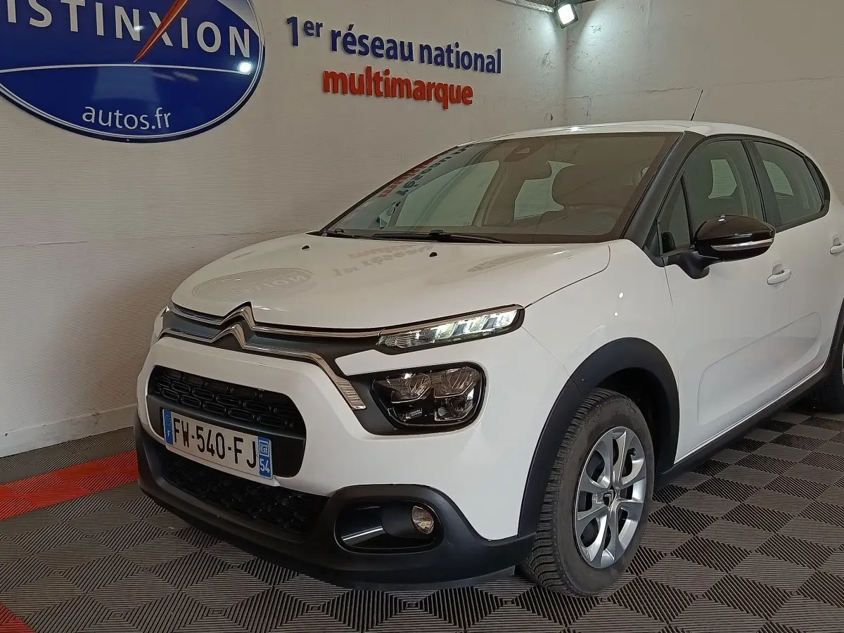 Citroën C3 blanche vue 3/4 avant droit en intérieur, avec phares LED et rétroviseurs noirs brillants.
