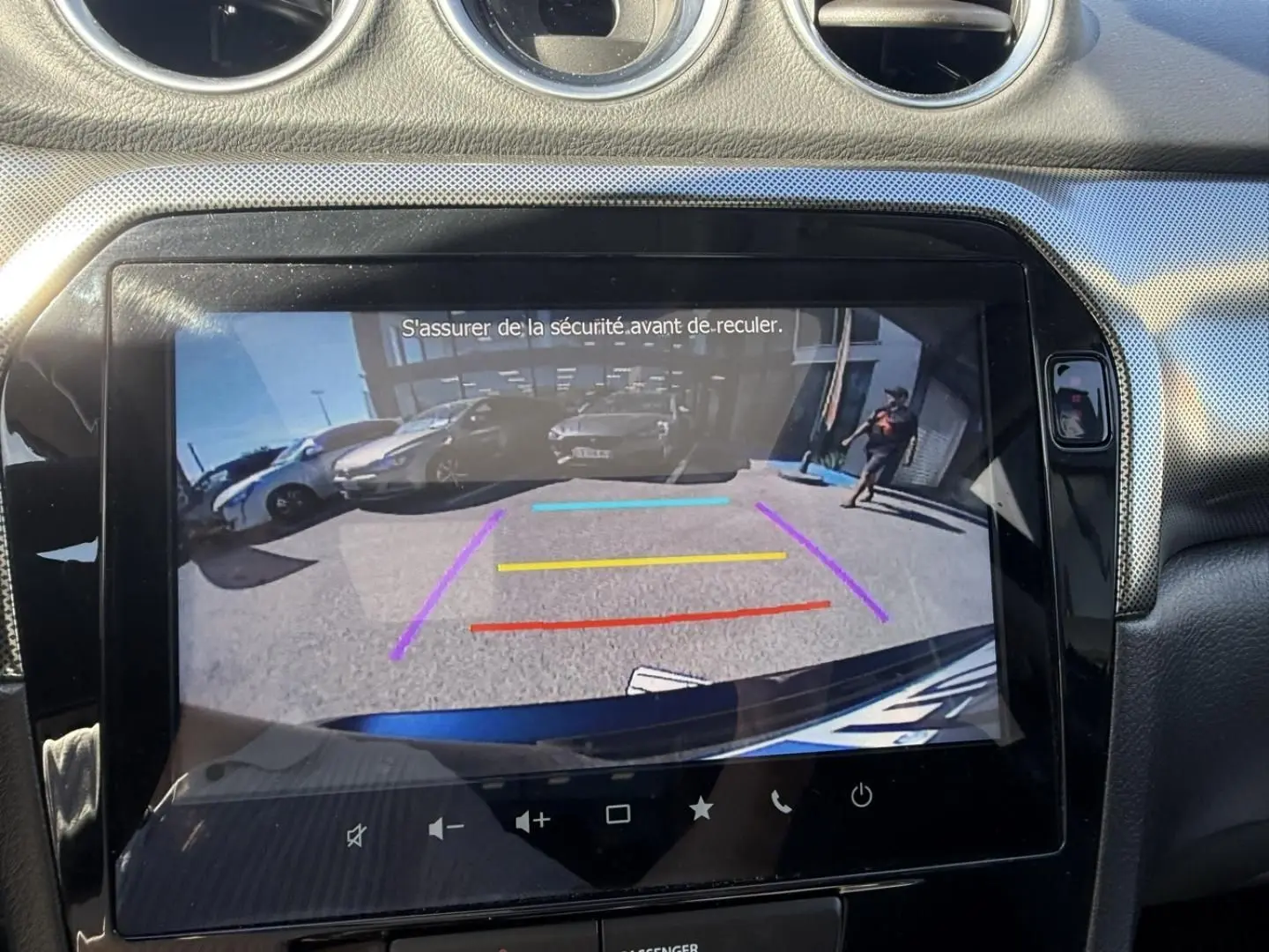 Vue de l'écran de recul du Suzuki Vitara bleu foncé métal 2025, avec lignes de guidage colorées et environnement arrière visible.