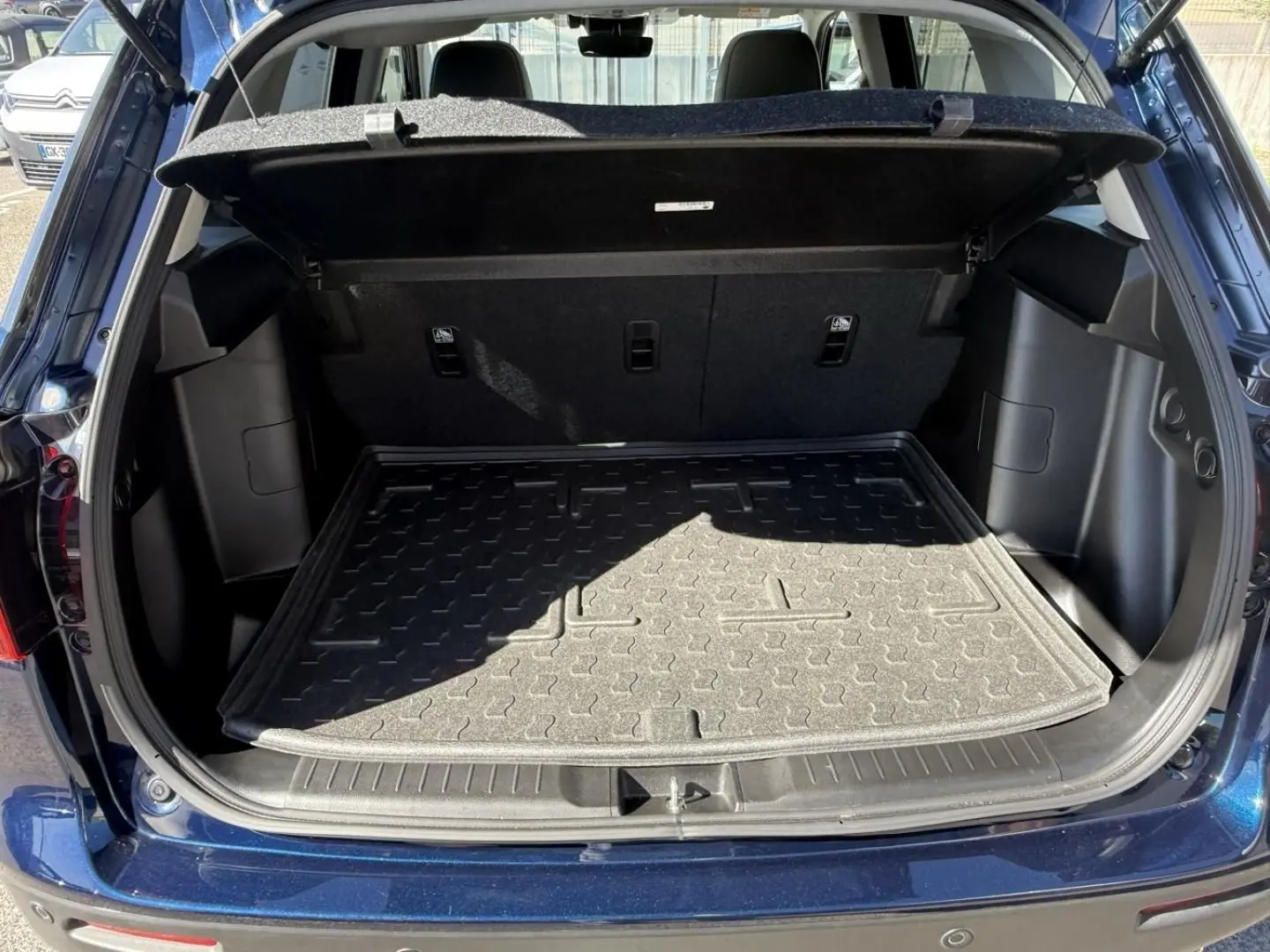 Coffre ouvert vu de l'arrière d'un Suzuki Vitara 2025 bleu foncé métal, montrant le tapis de coffre et l'intérieur spacieux.