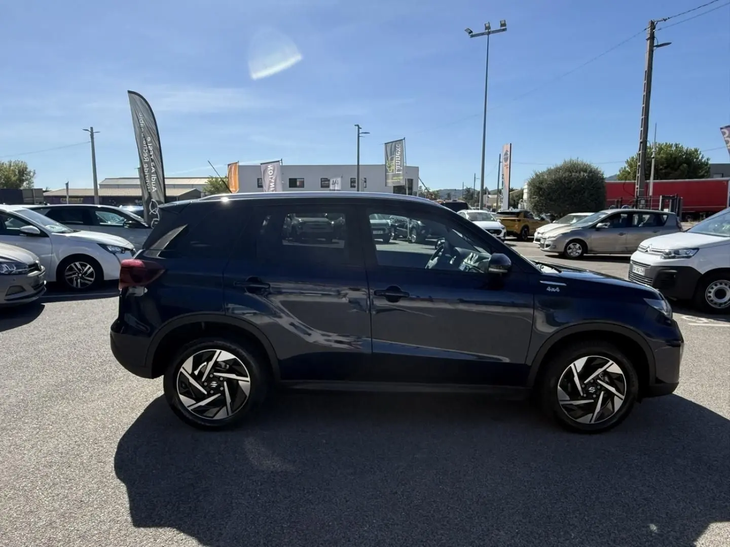 Suzuki Vitara 2025 bleu foncé métal, vue de profil côté gauche, avec jantes alliage noires et badge 4x4 visible.