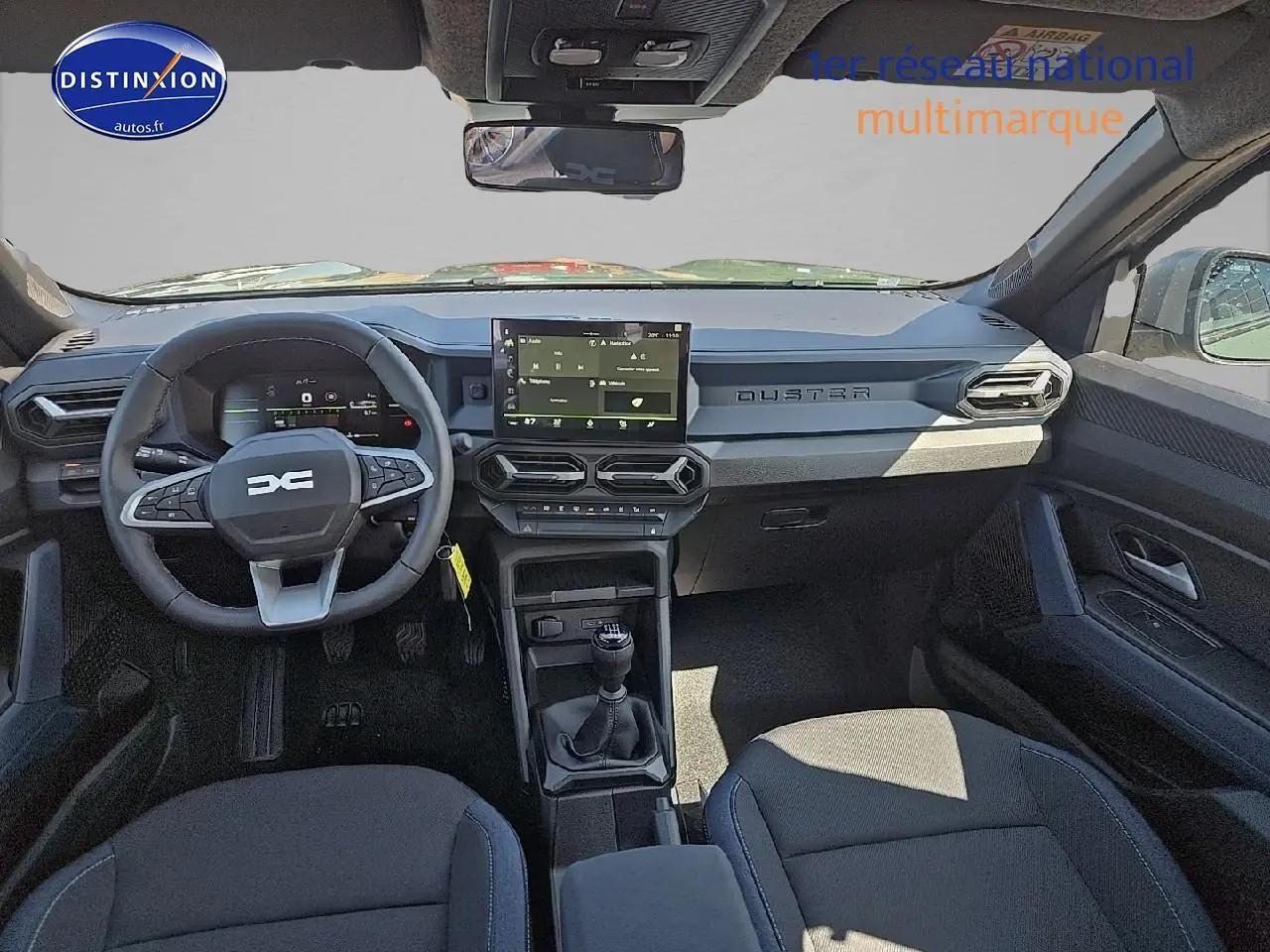 Intérieur avant du Dacia Duster 2025 avec tableau de bord moderne, volant multifonction et écran tactile central.