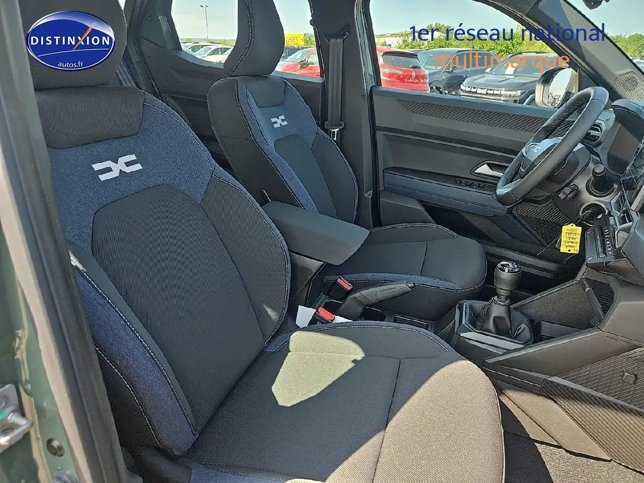 Intérieur du Dacia Duster 2025 vert kaki, vue côté gauche sur sièges tissu noir et bleu avec accoudoir central.