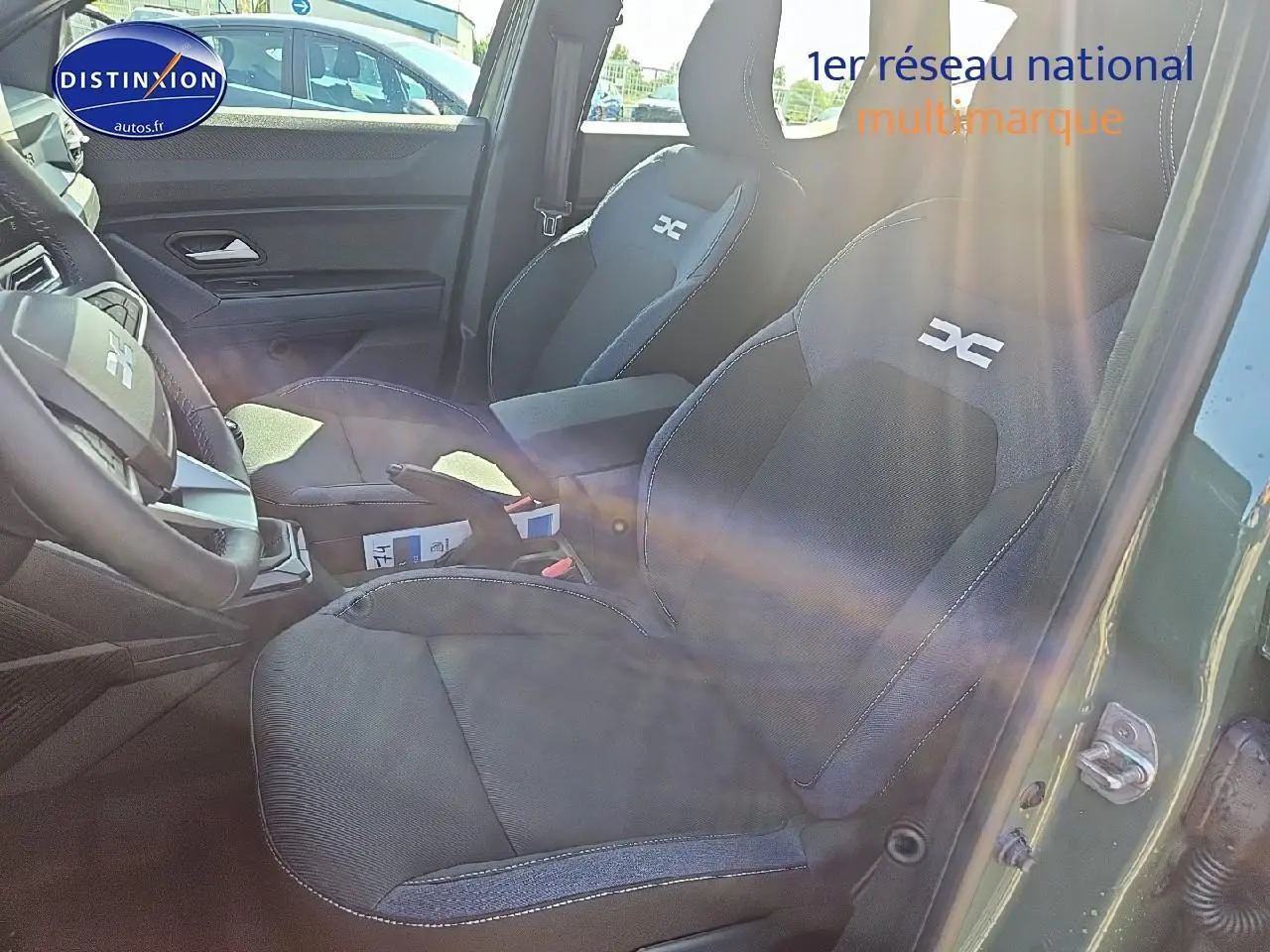 Intérieur du Dacia Duster 2025 vert kaki, vue côté droit sur sièges avant avec logo DC brodé et accoudoir central.