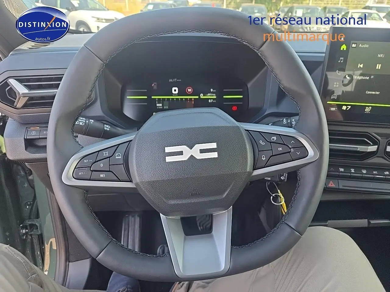 Vue intérieure centrée sur le volant multifonction noir du Dacia Duster vert kaki 2025 avec tableau de bord digital et écran tactile.