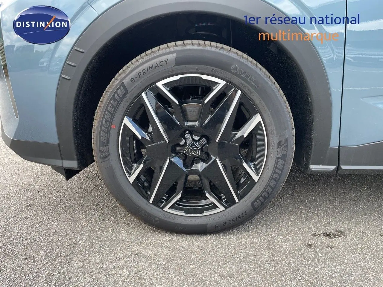 Gros plan sur la roue avant gauche du Peugeot 3008 Hybrid bleu Ingaro Metal avec jante noire et argentée.