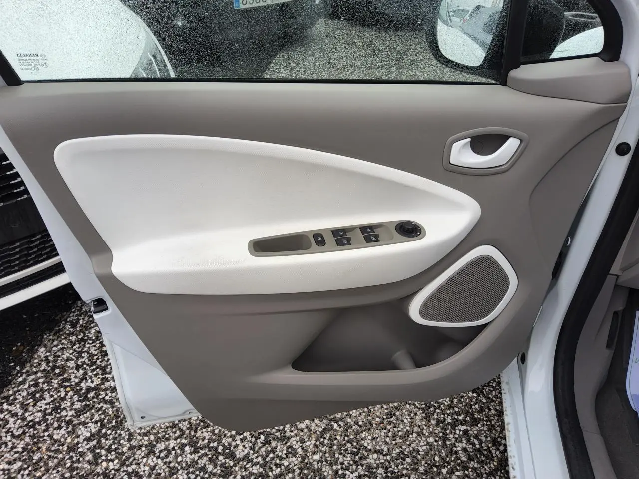 Porte avant gauche ouverte d'une Renault ZOE blanche, montrant le panneau intérieur beige et blanc avec commandes électriques.