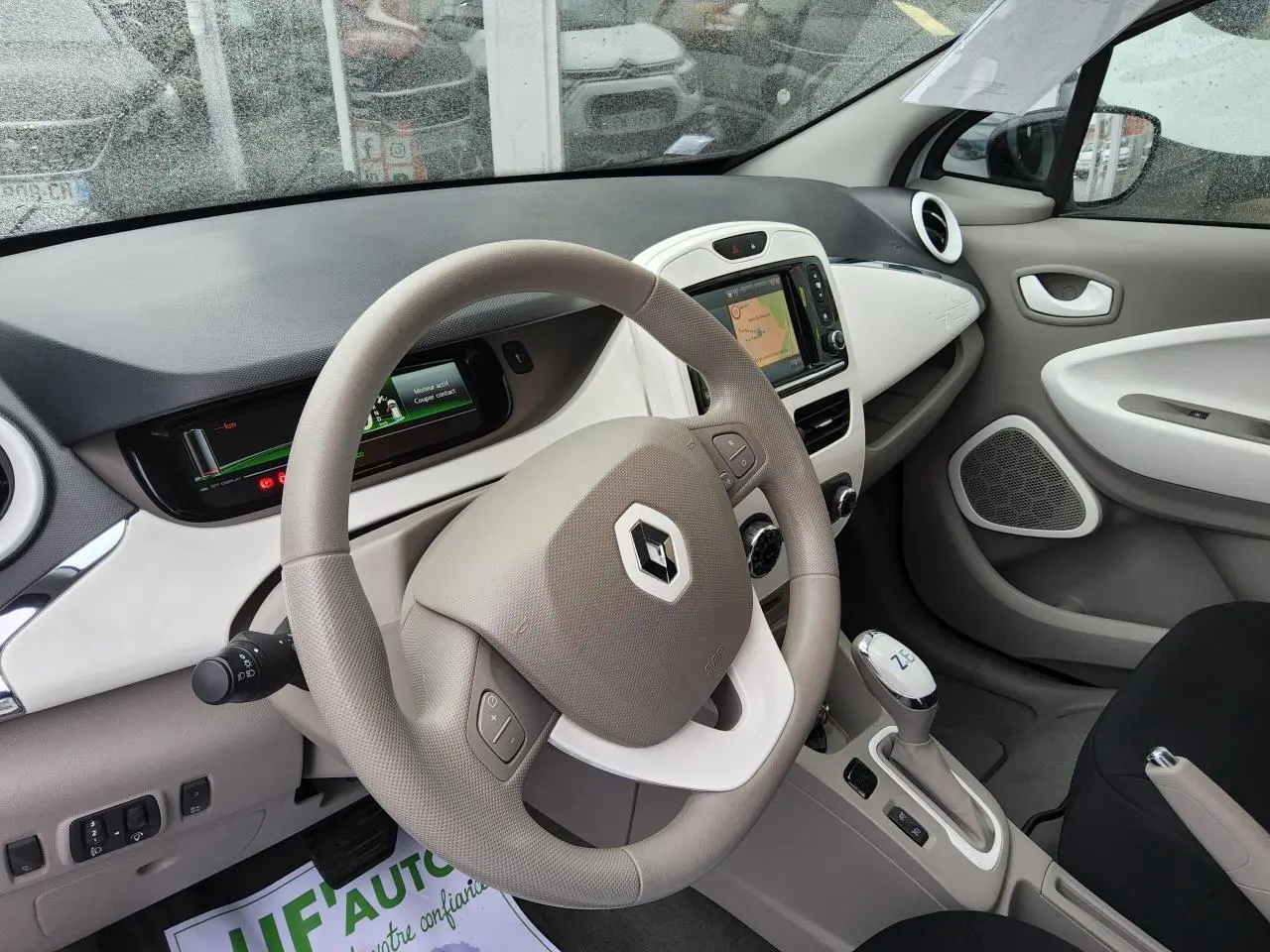 Intérieur de Renault ZOE blanc 2016 vu côté conducteur, volant beige avec logo Renault et console centrale moderne.