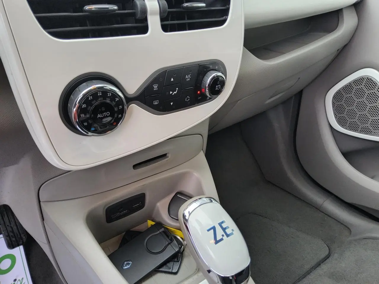 Gros plan sur la console centrale beige de la Renault ZOE blanche, avec levier de vitesse marqué Z.E. et commandes climatisation.