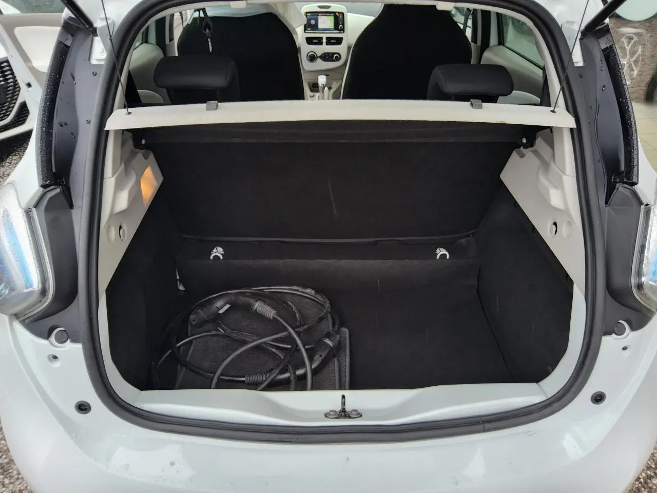 Coffre ouvert d'une Renault ZOE blanche vue arrière, avec câble de recharge électrique visible à l'intérieur.