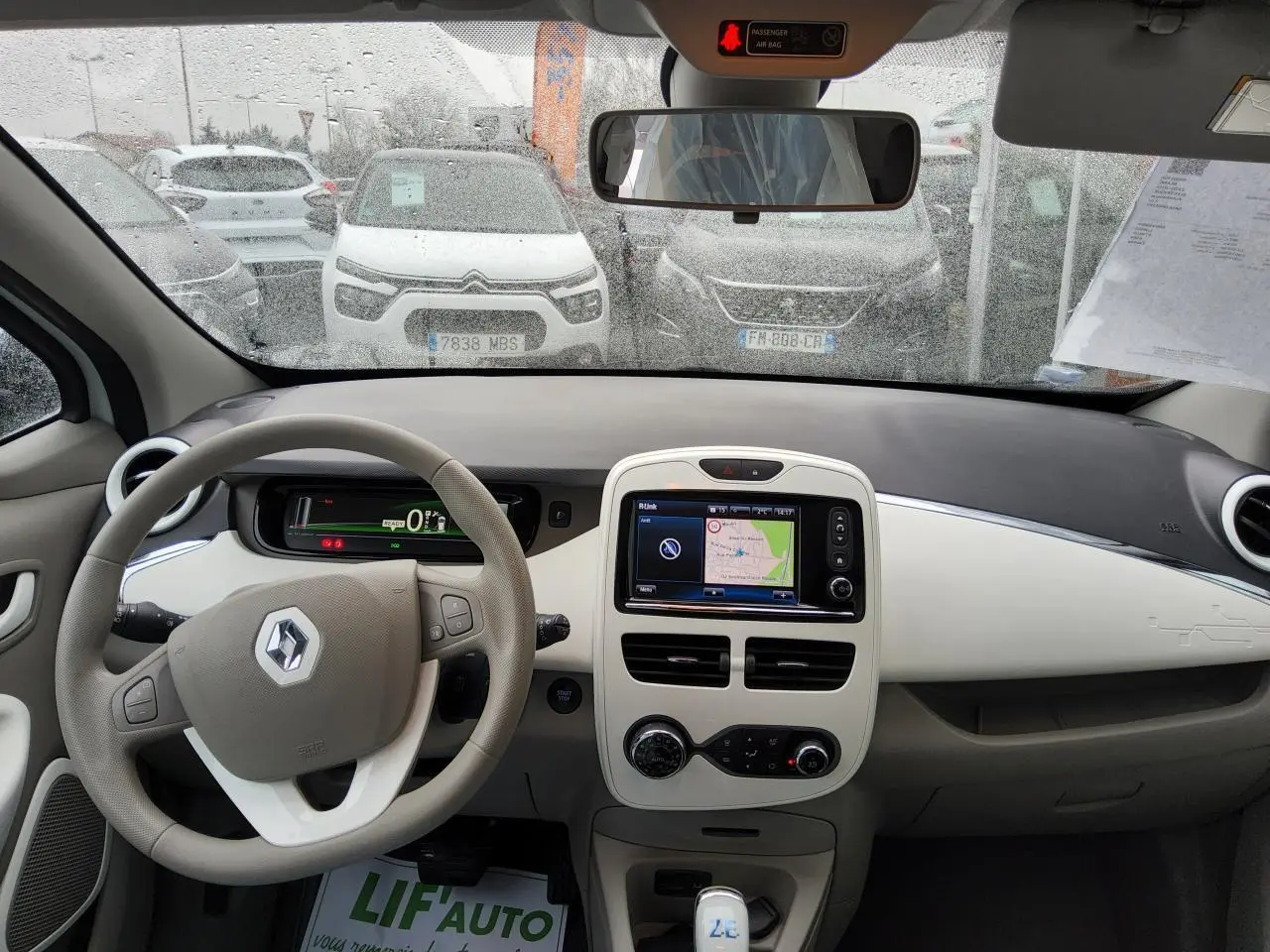 Vue intérieure frontale du tableau de bord beige et noir de la Renault ZOE Z.E. R240 Life avec écran tactile et volant multifonction.