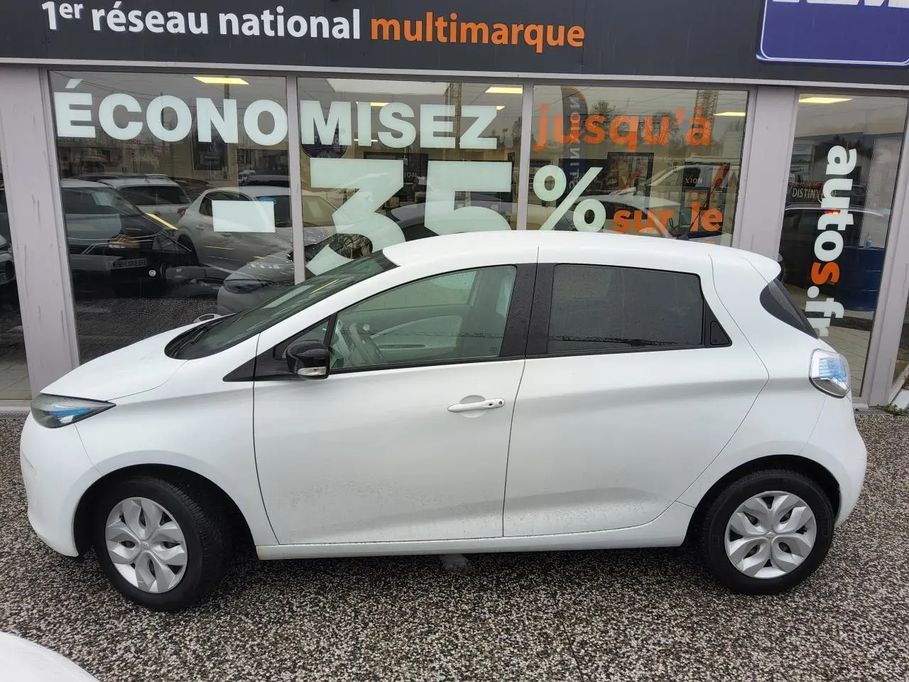 Profil côté gauche d'une Renault ZOE blanche Z.E. R240 Life, compacte avec vitres arrière surteintées et enjoliveurs 15 pouces.