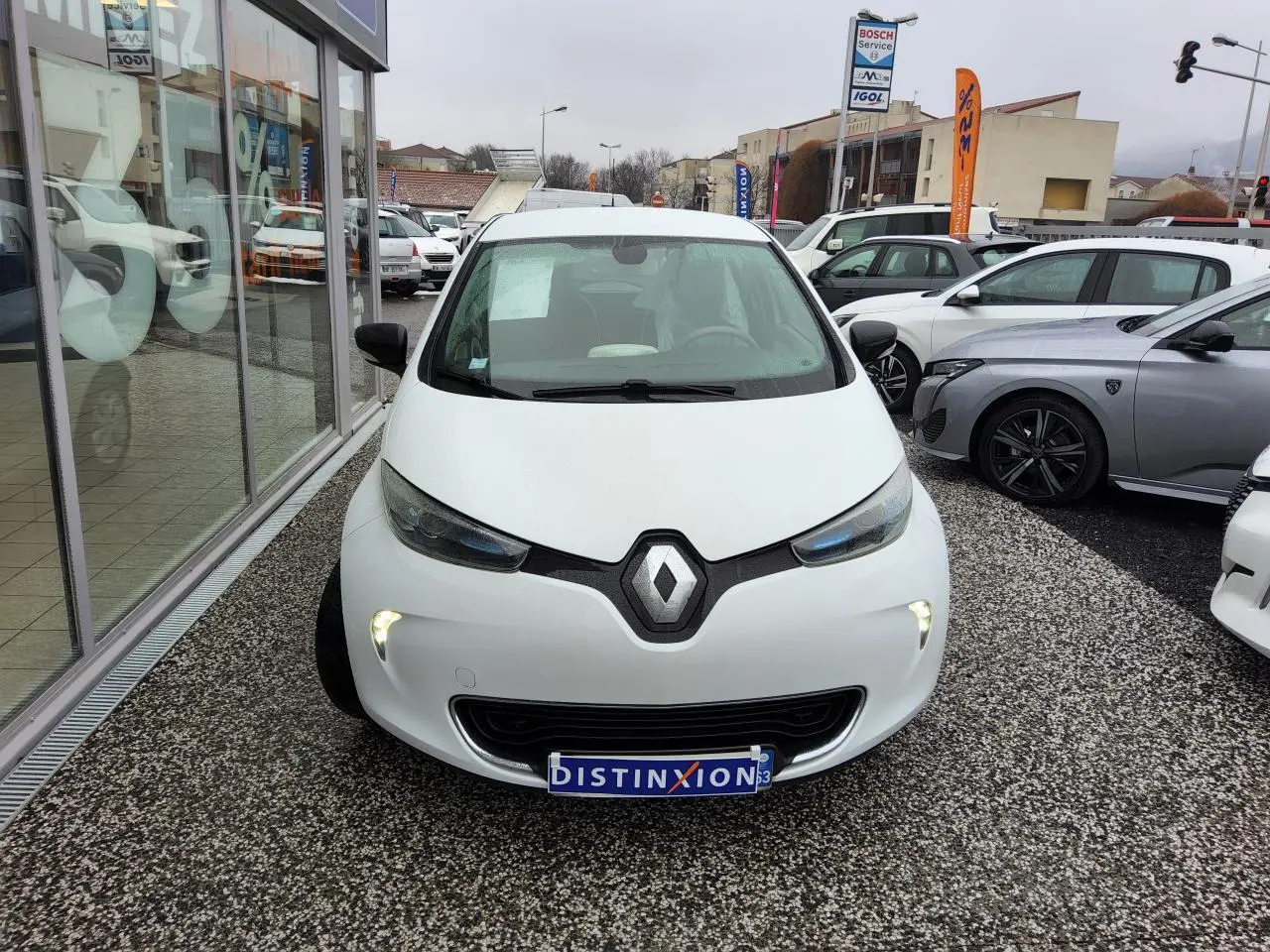 Vue avant d'une Renault ZOE blanche 2016 avec feux diurnes LED allumés sur un parking extérieur.