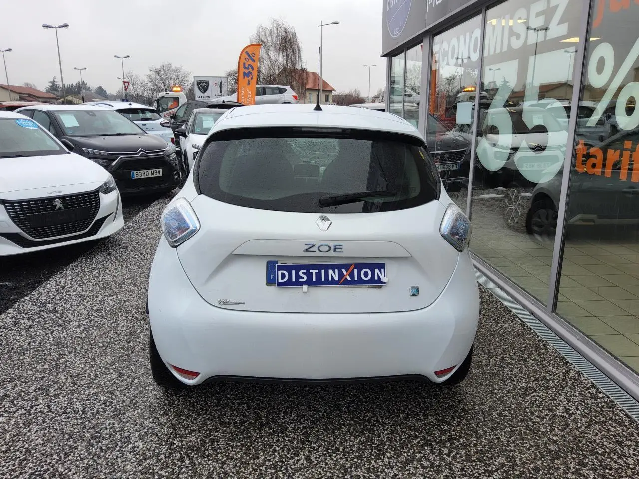 Vue arrière d'une Renault ZOE blanche 2016 avec badges ZOE et Z.E. sur un parking de concession.