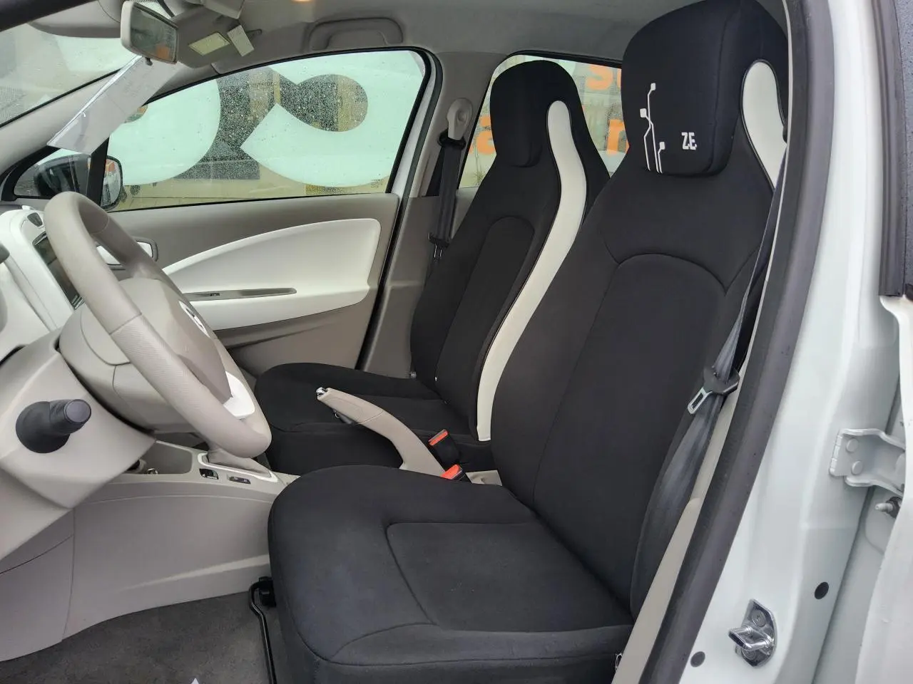 Intérieur de la Renault ZOE blanche vue côté gauche, sièges noirs avec logo Z.E. sur l'appuie-tête conducteur.