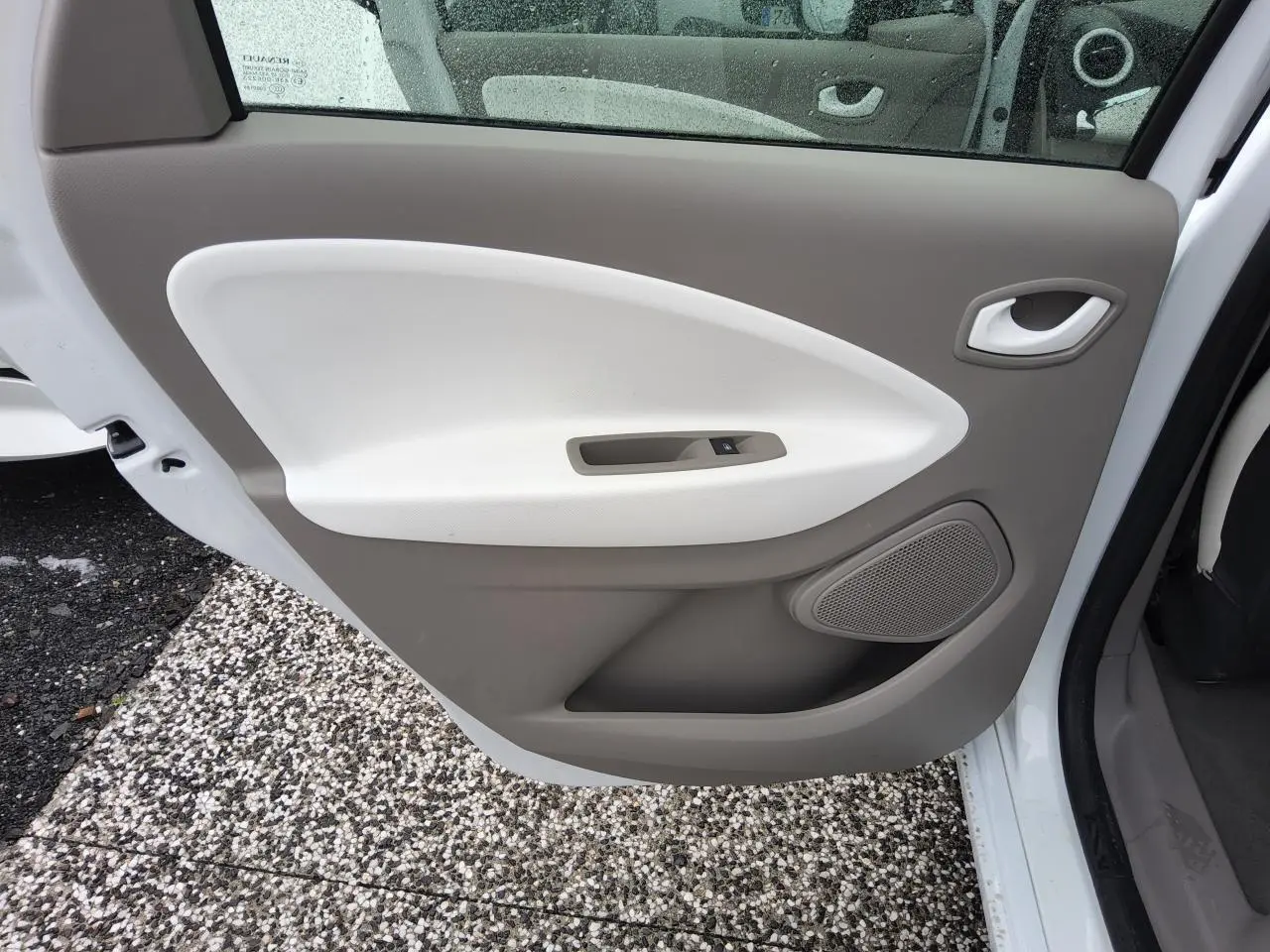 Porte arrière gauche ouverte de la Renault ZOE blanche, montrant le panneau intérieur beige et blanc avec commande de vitre.