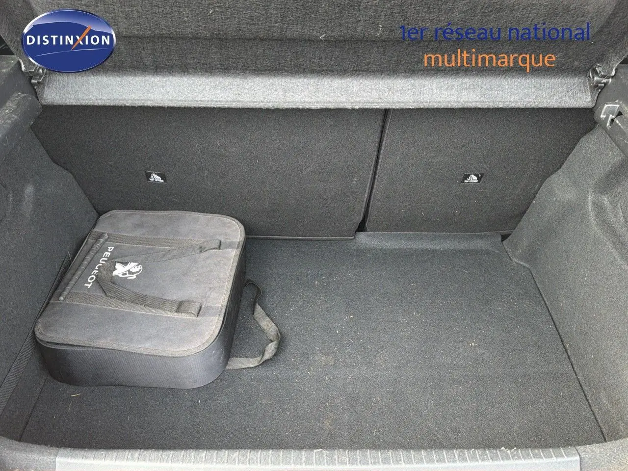 Coffre ouvert d'une Peugeot 208 électrique jaune Faro métal, montrant un sac Peugeot noir rangé à gauche.