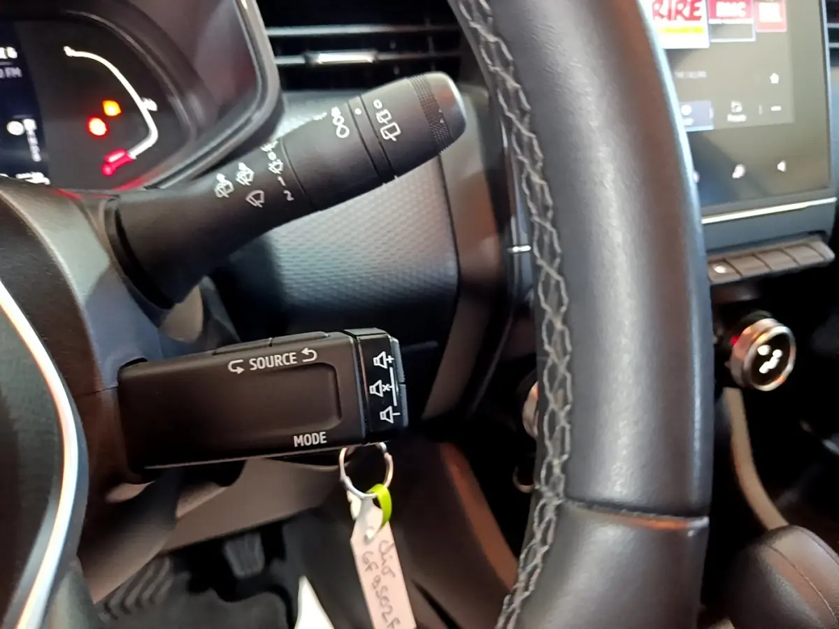 Gros plan sur le volant cuir et les commandes au volant d'une Renault Clio Business E-TECH 140 gris foncé, tableau de bord en arrière-plan.