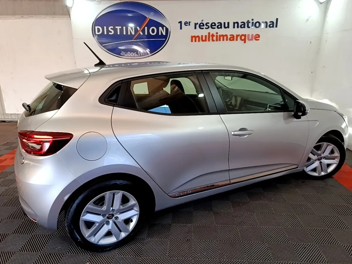 Vue latérale droite d'une Renault Clio gris clair 5 portes en intérieur sur sol damier noir et rouge.