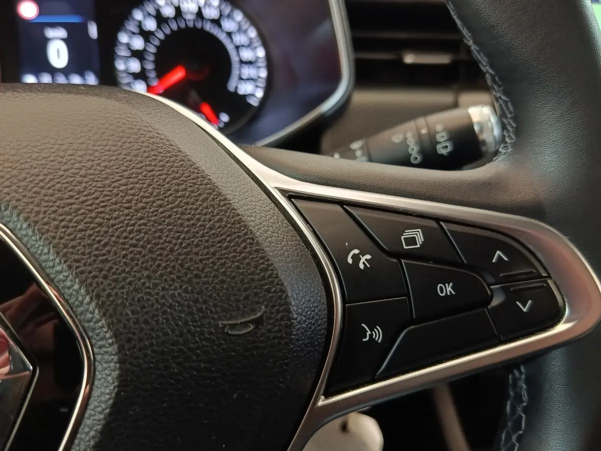 Gros plan sur le volant cuir synthétique de la Renault Clio Business blanc, avec commandes multifonctions et tableau de bord en arrière-plan.