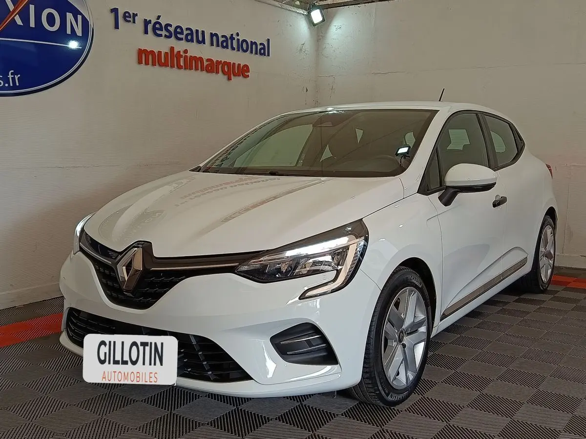 Renault Clio Business blanc vue 3/4 avant droit, avec phares LED et jantes alliage visibles en intérieur showroom.
