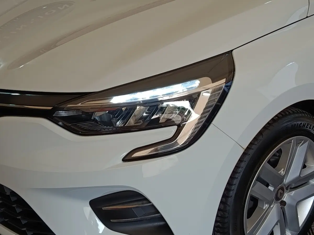 Gros plan sur l'avant droit blanc de la Renault Clio 2021, mettant en valeur le phare LED et la jante alliage.